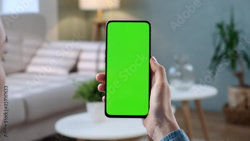 Close-up Shot of Young Woman at Home Sitting on a Chair using With Green Mock-up Screen Smartphone. Girl is Watcing Content Without Touching Gadget Screen. Modent Technology And Information Concept. photo