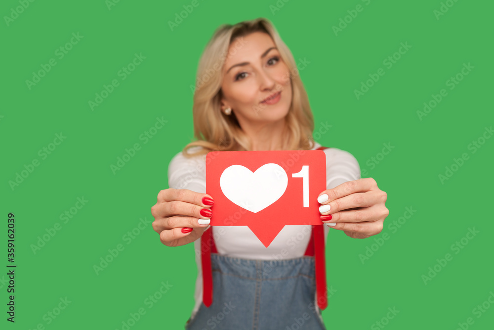 Push Like and follow social media blog. Portrait of lovely positive adult woman holding network heart icon, showing emoji notification button. indoor studio shot isolated on green background, closeup Push Like and follow social media blog. Portrait of lovely positive adult woman holding network heart icon, showing emoji notification button. indoor studio shot isolated on green background, closeup