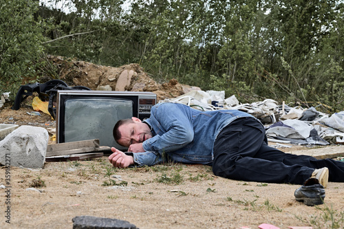 Photo of a caucasian homeless man lying in the trash. Environmental protection concept