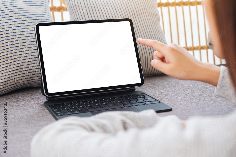 Mockup image of a woman using and pointing finger at tablet pc with blank desktop white screen as a computer pc on sofa at home Mockup image of a woman using and pointing finger at tablet pc with blank desktop white screen as a computer pc on sofa at home