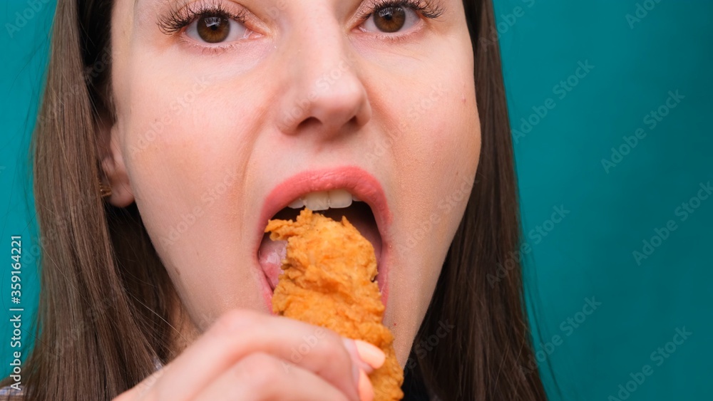 Young happy woman eating deep fried chicken, closeup. Woman eats chicken wings, calorie intake and health risks, cholesterol