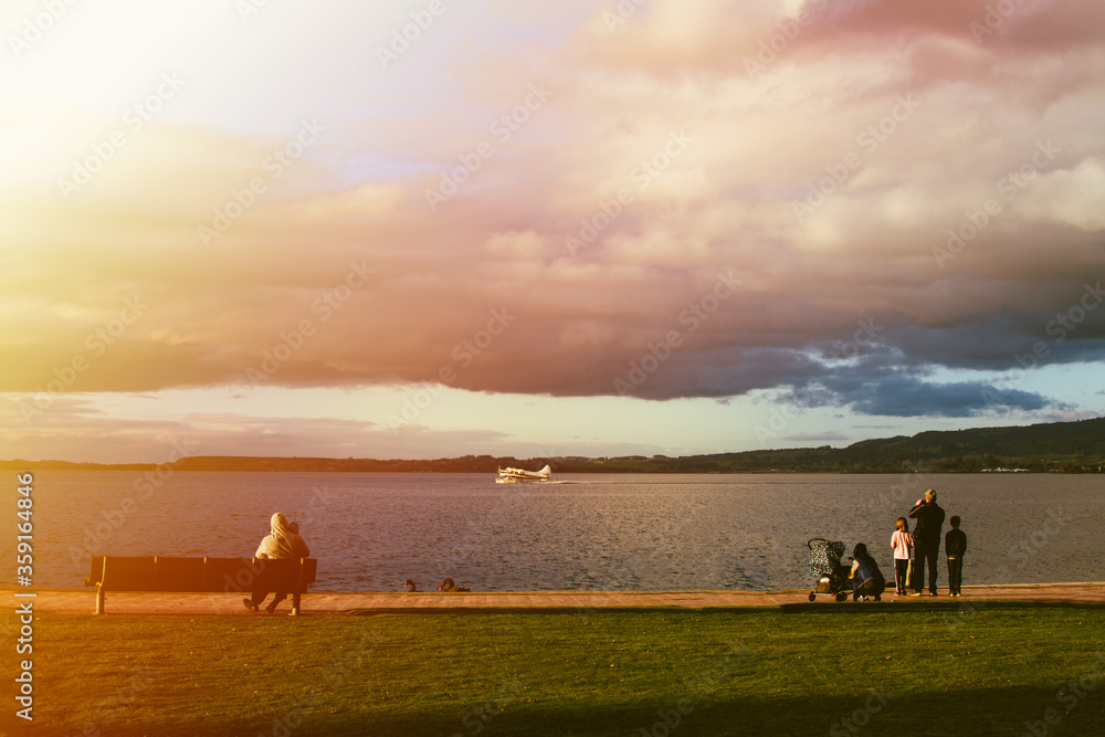 Young families watching a seaplane speeding up to take off from the lake Rotorua at sunset