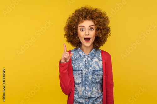 Eureka, I know answer! Portrait of amazed inspired woman with curly hair pointing finger up and having genius idea, surprised by sudden clever solution. studio shot isolated on yellow background photo
