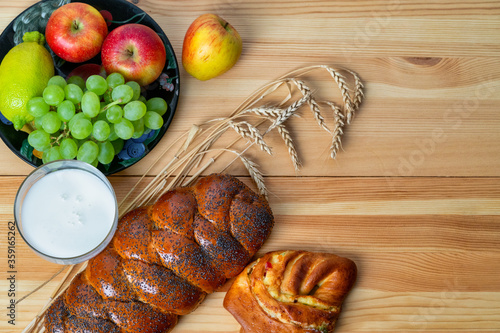 Wicker bun, lemon, apples, green grapes, wheat and a glass with milk on a wooden table. Jewish holiday Shavuot. photo