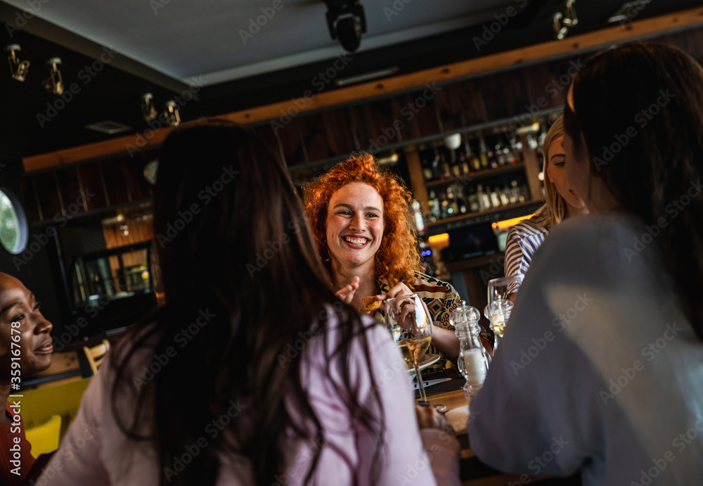 Fototapeta premium Group of young female friends having fun in restaurant, talking and laughing while dining at table.