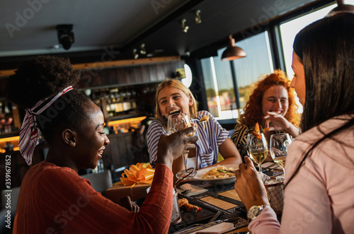 Group of young female friends having fun in restaurant  talking and laughing while dining at table.