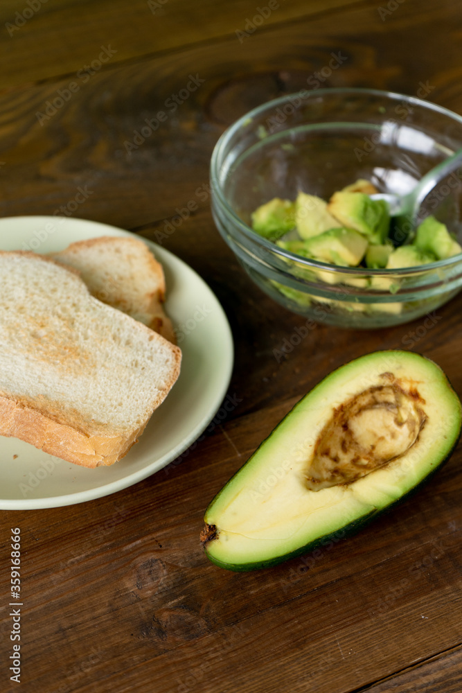 Fried bread for toasts and avocado for breakfast in the morning on brown woodwn table. Vretical Fried bread for toasts and avocado for breakfast in the morning on brown woodwn table. Vretical