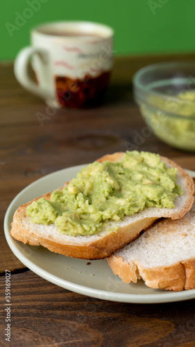 Tasty toasts with avocado and a cup of coffee for breakfast on plate on brown wooden table and green background. Vertical. 