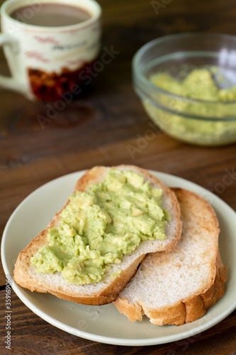 Tasty toasts with avocado and a cup of coffee for breakfast on plate on brown wooden table. Vertical. 