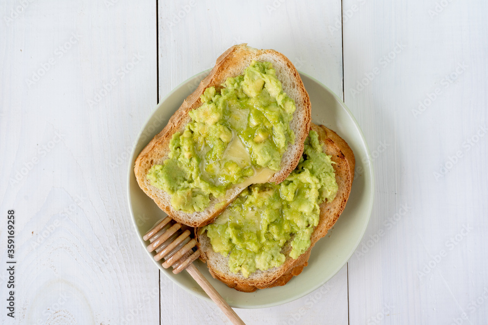 Tasty fresh toasts with avocado and honey for breakfast on plate on white wooden table. Top view Tasty fresh toasts with avocado and honey for breakfast on plate on white wooden table. Top view