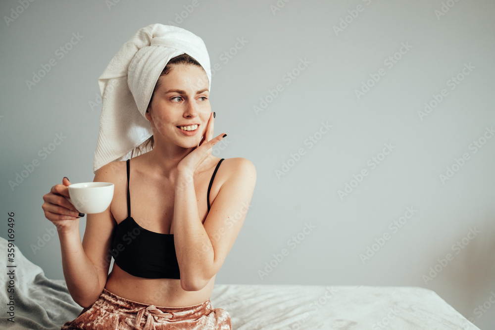 Portrait of Beautiful Young Caucasian White Adult Girl in Bath Towel Sitting on the Bed with Cup of Coffee Portrait of Beautiful Young Caucasian White Adult Girl in Bath Towel Sitting on the Bed with Cup of Coffee