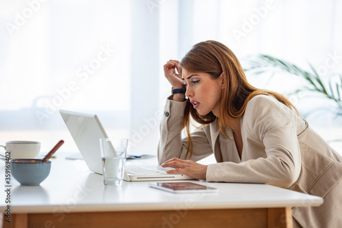 Depressed businesswoman rubbing eyes in office. Portrait of depressed young businesswoman sitting at computer in office rubbing eyes. Overworking concept