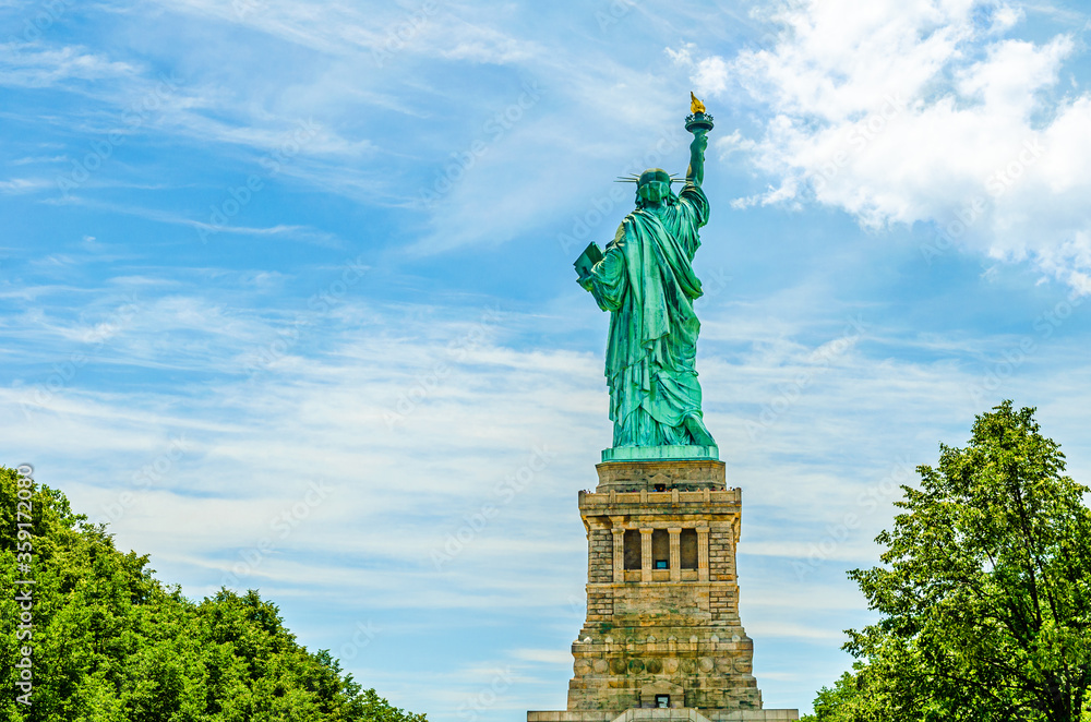 The back of the outdoor Statue of Liberty on a background of blue sky with white clouds on Liberty Island, New York City, USA