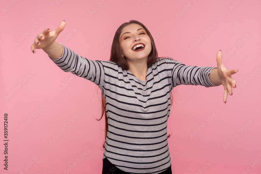 Come into my arms! Portrait of hospitable excited friendly woman in striped sweatshirt raising hands to embrace, welcoming guests with charming pleased smile. studio shot isolated on pink background Come into my arms! Portrait of hospitable excited friendly woman in striped sweatshirt raising hands to embrace, welcoming guests with charming pleased smile. studio shot isolated on pink background