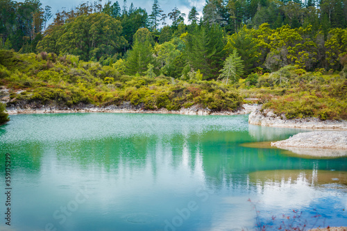Turquoise water of geothermal lake refelcts blue sky and surrounding forest photo