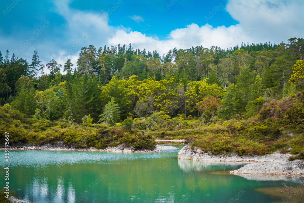Turquoise water of geothermal lake quietly reflects blue sky and surrounding forest