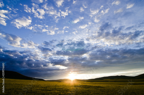 Beautiful dramatic summer sunset with scattered clouds and sun touching the horizon on a crops meadow, Mongolia