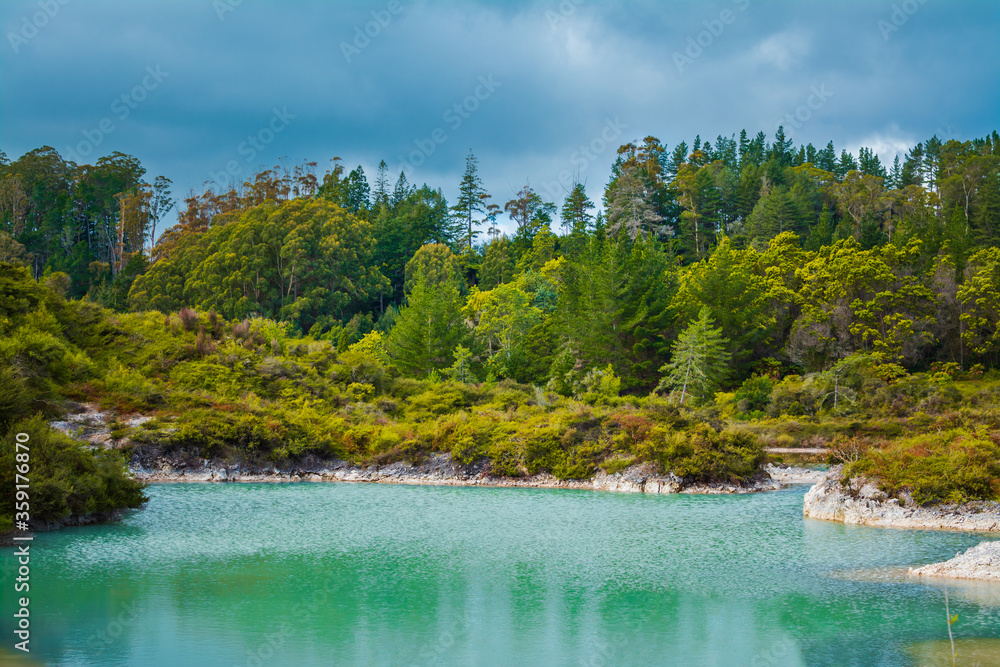 Turquoise waters of geothermal lake amongst low trees and shrubbery