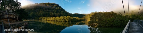 Beautiful morning panoramic view of Cockle creek with reflections of blue sky, foggy mountains and trees, Mangrove boardwalk, Bobbin Head, Ku-ring-gai Chase National Park, New South Wales, Australia 