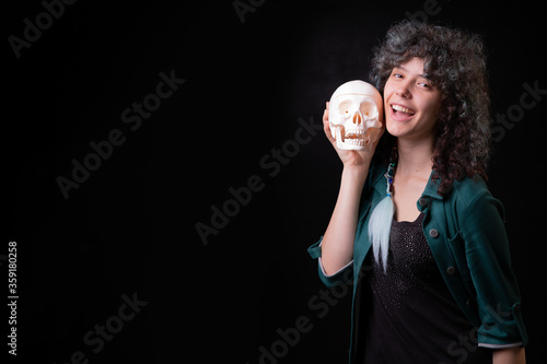 beautiful young curly girl on a black background holds a skull in her hands and rejoices, smiles, has fun