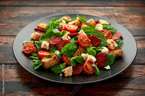 Chorizo Tomato salad with spinach, feta cheese and croutons on black plate. healthy summer food