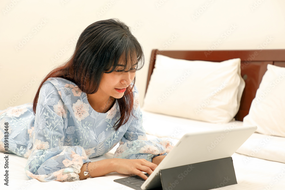 young Asian Malay Muslim woman wearing baju kurung dress at home on bed study work on computer tab young Asian Malay Muslim woman wearing baju kurung dress at home on bed study work on computer tab