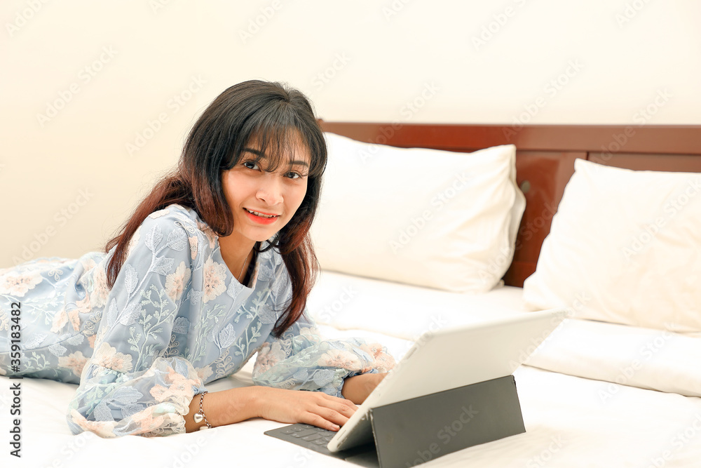 young Asian Malay Muslim woman wearing baju kurung dress at home on bed study work on computer tab look at camera young Asian Malay Muslim woman wearing baju kurung dress at home on bed study work on computer tab look at camera