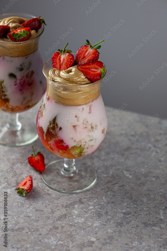 Cold summer dessert. Bowls of layered jelly served on table against light background. Colourful, festive cocktail with sweets jelly in glass. Strawberries, yogurt and chocolate cream close-up. Cold summer dessert. Bowls of layered jelly served on table against light background. Colourful, festive cocktail with sweets jelly in glass. Strawberries, yogurt and chocolate cream close-up.
