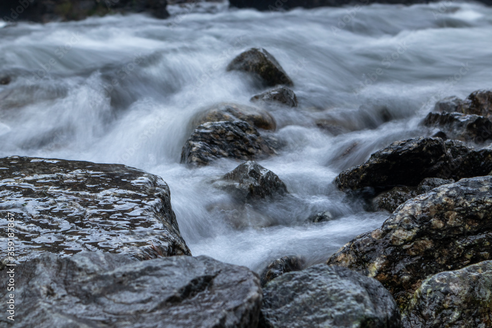 River near Latefossen waterfall on long exposure in dark cloudy moody weather light. Soft silky water on dark wet rocks