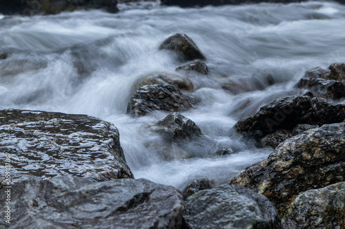 River near Latefossen waterfall on long exposure in dark cloudy moody weather light. Soft silky water on dark wet rocks