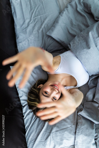 Top view of a young attractive woman hands in camera stretching hands while lying in bed in the morning