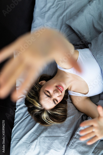 Top view of a young attractive woman sad fae dont want to wake up hands in camera stretching hands while lying in bed in the morning