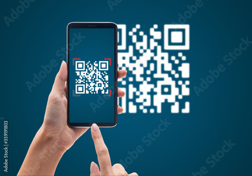 Hand using mobile smart phone scan Qr code on blue background. Cashless technology and digital money concept. photo