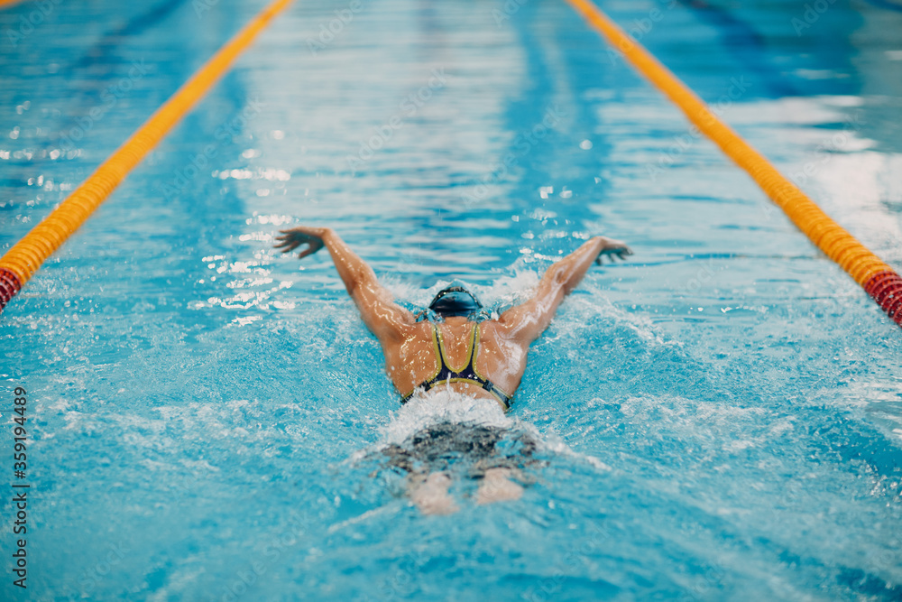 Young woman swimmer swims in swimming pool. Back view.