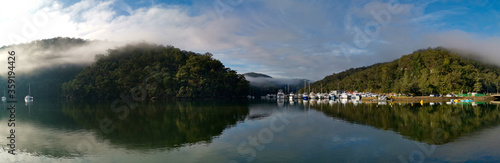Beautiful morning panoramic view of Cockle creek with reflections of blue sky, light clouds, foggy mountains and trees, Bobbin Head, Ku-ring-gai Chase National Park, New South Wales, Australia