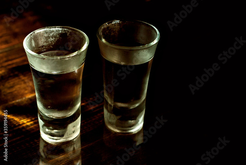 Two frozen glasses close up. Glasses with alcohol on a black wooden table. Vodka on a dark contrasting background.