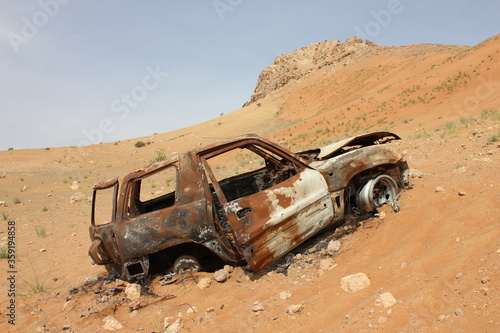 Burnt out wreckage of a SUV (4-wheel-drive) vehicle rusts away in hot and arid desert sand dunes terrain in Sharjah emirate in the United Arab Emirates.  