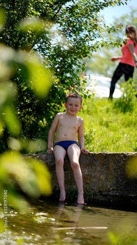Portrait of a funny little boy sitting near water outdoors