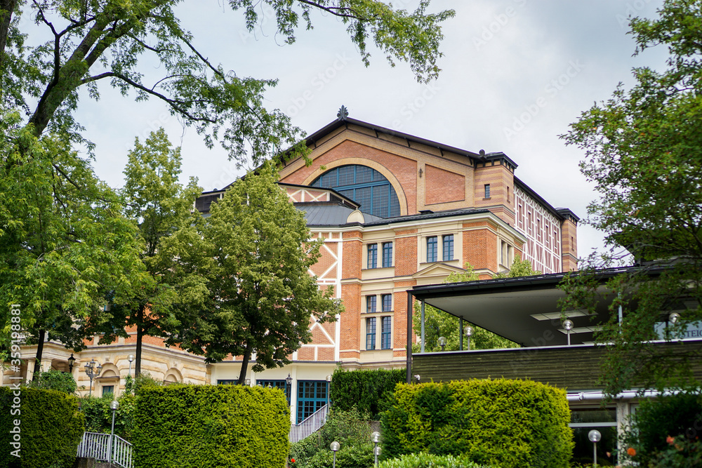 Sicht auf die Vorderansicht des Wagner Festspielhaus Bayreuth aus der Sicht des Parks. Bäume und Halle im Bild, blauer bewölkter Himmel.  Bayern, Deutschland.
