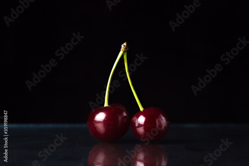 Cherry on a black background. Two red cherries on one branch
