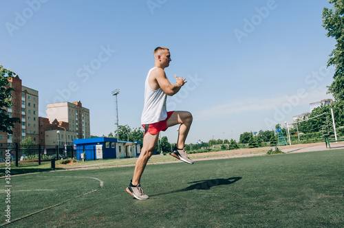 The athlete makes lunges, exercise to warm up before training. Male bodybuilder trains on sports ground. Full stadium plan