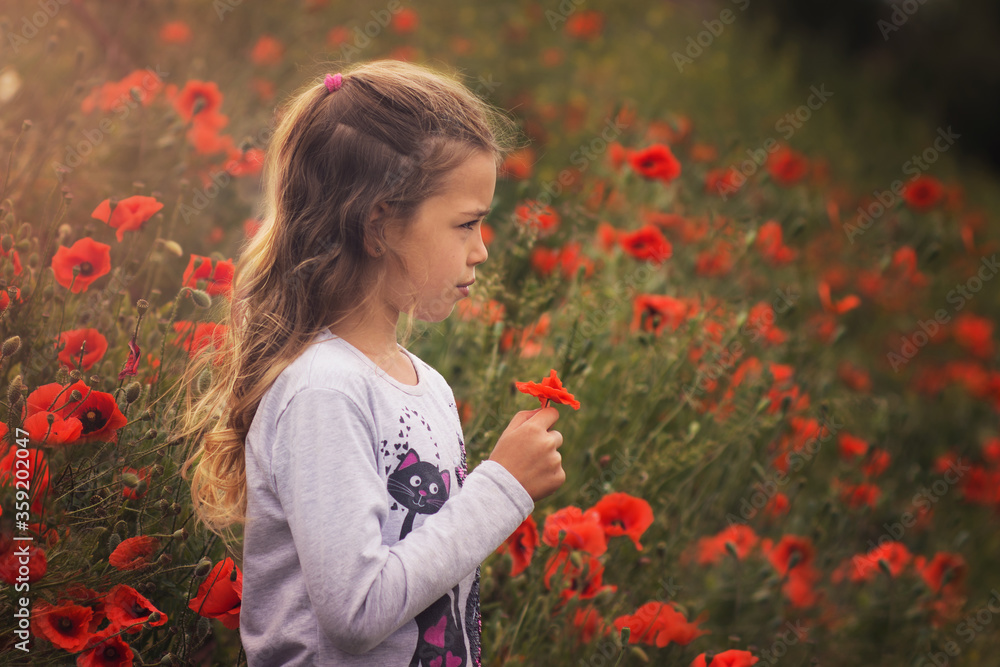 Naklejka premium dark portrait of young girl with red field poppy, kid in sunset with poppy