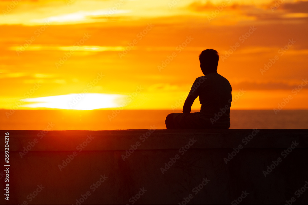 a man sitting on the shore of the ocean at sunset and meditating a man sitting on the shore of the ocean at sunset and meditating