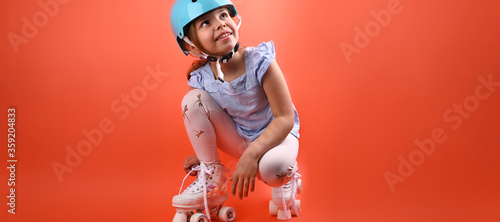 A small child with roller skates and a blue helmet demonstrates positive emotions A girl of 7 years old poses and prepares for active leisure on retro ice skates. Children's sport concept. Copy space.