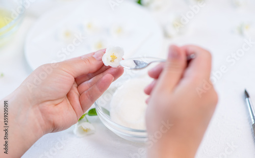 The cook   s hands hold a jasmine flower in their hands and use a spoon to pour sugar on the iced flower. Decor for cake concept.