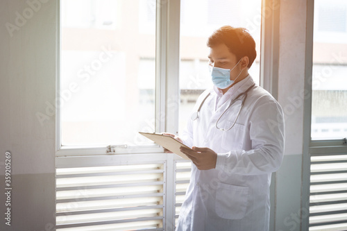 Portrait of a young cheerful and handsome doctor checking patient information and symptoms through tablet and patient documentation. Young confident male doctor portrait.