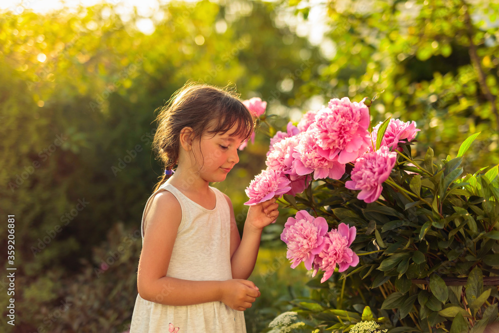 Little girl in the garden with pink peonies. Little girl in the garden with pink peonies.