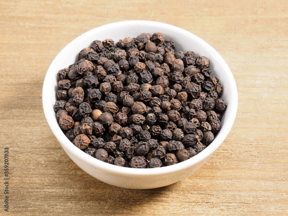 Spice black pepper in white bowl on brown wood background Spice black pepper in white bowl on brown wood background