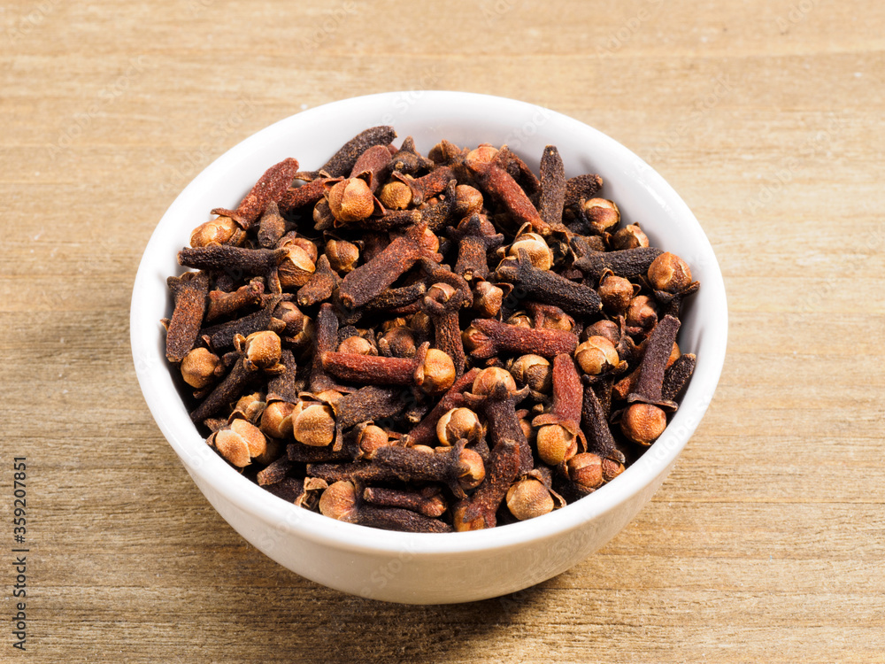 Spice cloves in white bowl on brown wood background. Healthy eating, ayurveda, naturopathy concept Spice cloves in white bowl on brown wood background. Healthy eating, ayurveda, naturopathy concept