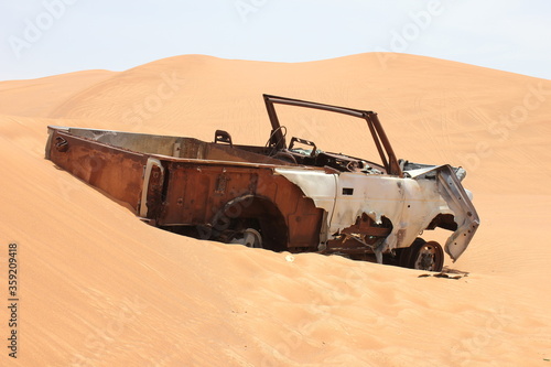 Burnt out wreckage of a SUV (4-wheel-drive) vehicle rusts away in hot and arid desert sand dunes terrain in Sharjah emirate in the United Arab Emirates.  